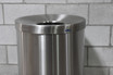 Sleek jumbo lobby waste receptacle by Frost in stainless steel, featuring a round top opening for convenient disposal, ideal for handling large volumes of waste in commercial settings. Next to a wall