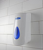 The Frost 707 white manual liquid soap/sanitizer dispenser mounted on a tiled wall, with a distinctive blue window indicating the soap level, ready for use.