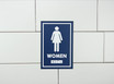 Frost 961 female washroom signage in a bold blue with white pictogram and Braille, ensuring clear and accessible directions for women's restrooms.