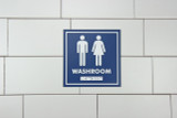 Frost 965 gender-neutral washroom signage in blue with white symbols and Braille, indicating a welcoming space for users of any gender.