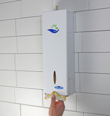 Customer using the Frost 614 free retail napkin dispenser in white, mounted on a tiled wall, demonstrating the ease of the hand-pull mechanism. On wall.