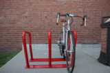 The durable and secure Frost 2090-Red steel bike rack, capable of accommodating six bicycles, stands out in a bold red, perfect for enhancing outdoor communal areas.