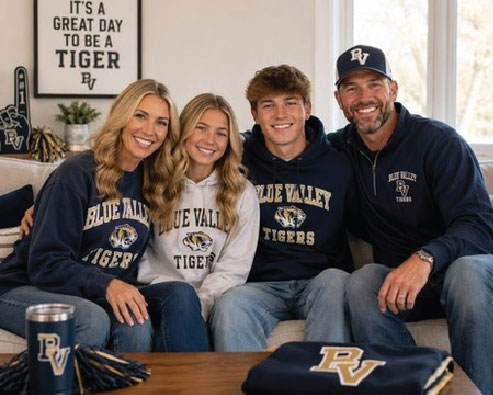 A family of four at home in matching navy Blue Valley Tigers spirit wear, with a school tumbler and pom-poms on the table.