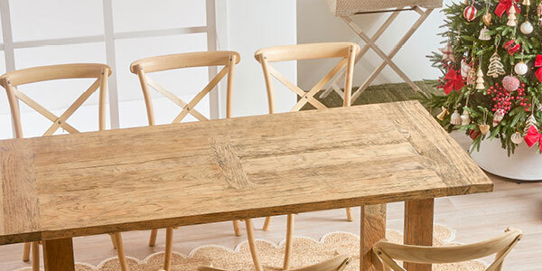 A wooden table with nothing on it and chairs surrounding it sit in the middle of the image, with a Christmas tree to the right of the room. 
