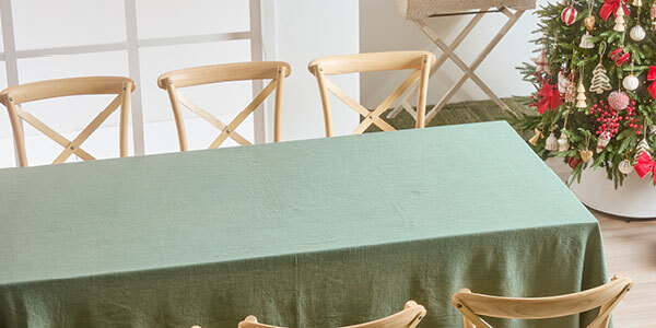 A table with a green table cloth sits in the middle of the image, with chairs around it and a Christmas tree in the far right corner of the room. 