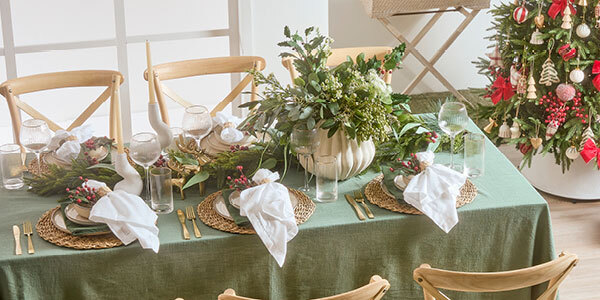 A table is set with a Christmas table setting with a Christmas tree in the background. 