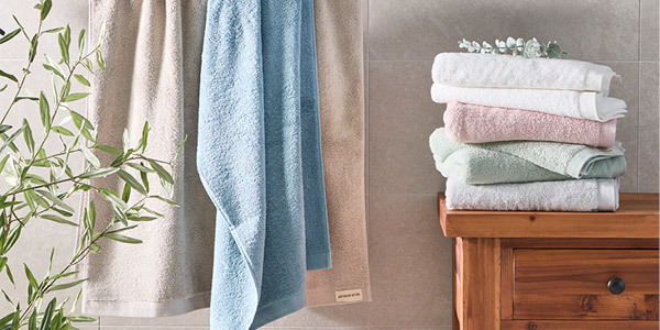 Australian Cotton Towels hang on a towel rail on the right and are folded in a stack on the left of the image