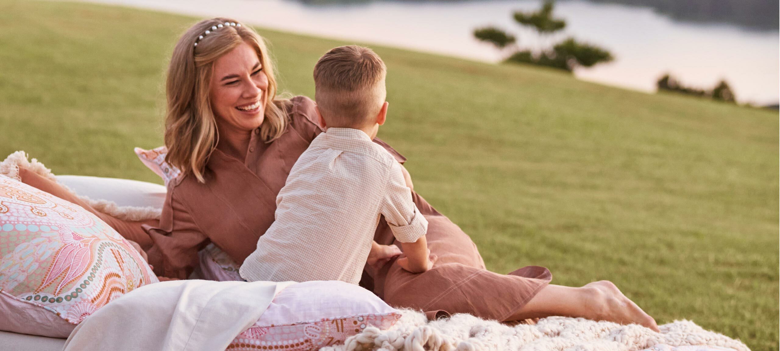 Domica Hill, a blonde woman, is lying on a bed smiling at her son. 