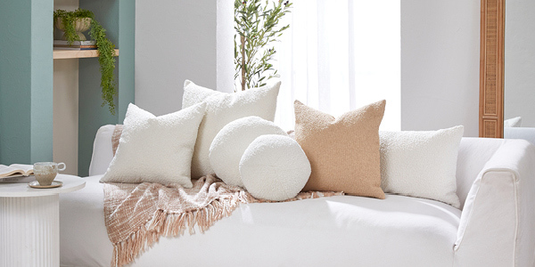 A range of different sized cream boucle cushions sit on a couch. 