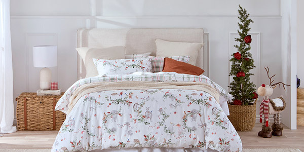 Picture features a bed with Australian Christmas themed bedding. Next to it is a slimline Christmas tree decorated with Australian native flowers. 