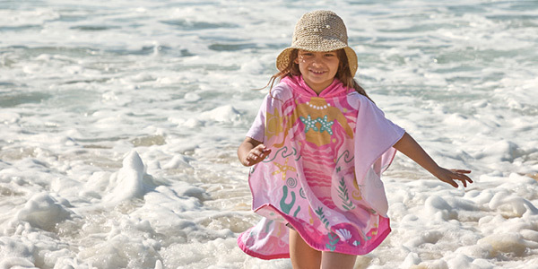 Child wearing kids hooded beach towel and hat playfully runs away from the waves at the beach