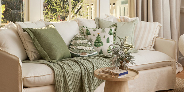 A couch featuring natural and green cushions, including Christmas cushions.