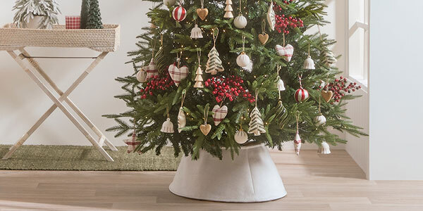 A Christmas tree decorated with lights, holly berry stems, base decorations and a Christmas tree skirt.
