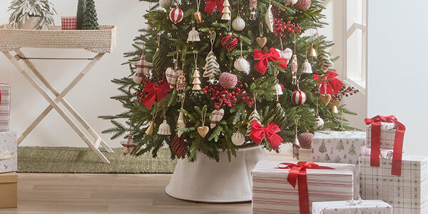 A decorated Christmas tree with a white tree skirt sits behind a pile of wrapped presents. 
