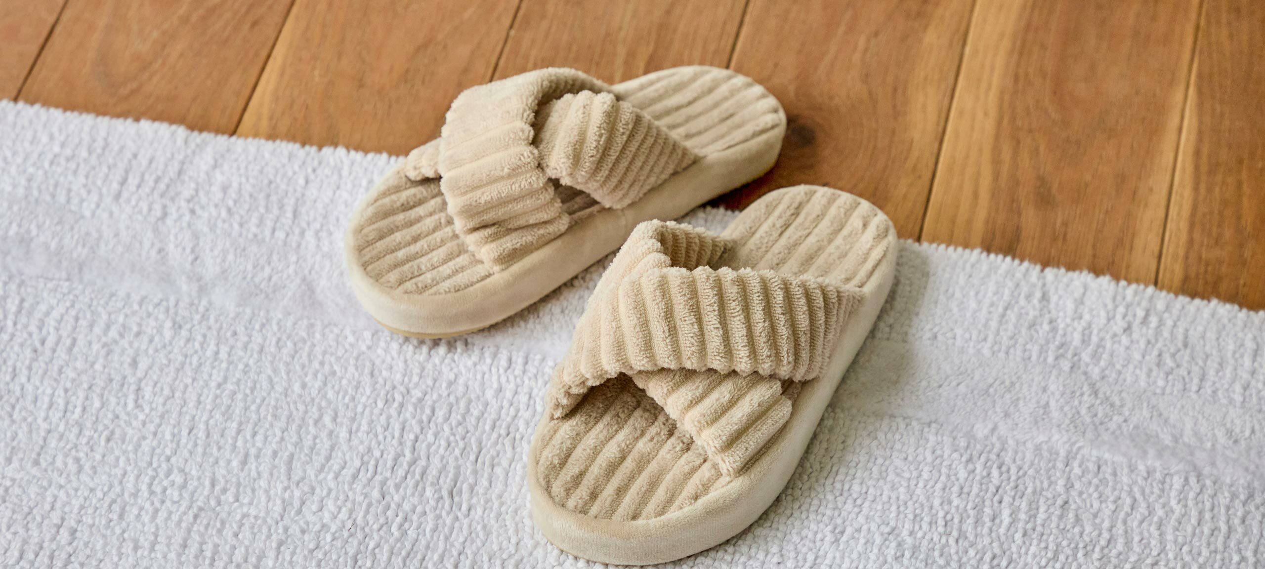 Plush neutral toned slippers sit atop a bath mat