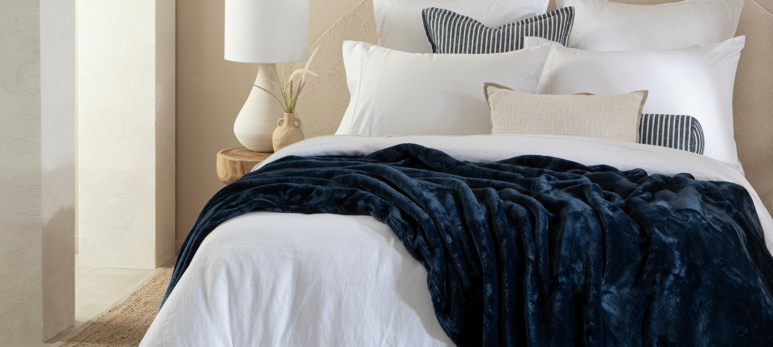 A plush navy blue blanket is draped across a bed with white and blue bedding and cushions. 