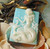 Beach City Boutique A close-up image of a handcrafted bar of mermaid soap featuring intricate seahorse and ocean wave designs. The soap is vibrant in color, with shades of blue and green reminiscent of the ocean.