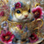 Elly AI small hamster sitting inside ornate teacup surrounded by flowers with soft pastel tones