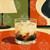 Creamy coffee cocktail with ice cubes in a modern lowball glass set against retro mid-century modern décor by 1000 No Kotoba.
