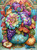 Elegant autumn floral arrangement with colorful dahlias, pumpkins, grapes, pears and fall foliage displayed in an ornate teal vase with blue birds.
