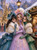 Three elegant women in teal, lavender, and green vintage gowns with white fur wraps at a snowy Christmas market with glowing lights and Christmas tree.