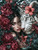 Dark-haired woman beside a blue-eyed white tiger surrounded by burgundy peonies, coral hibiscus flowers, and dark tropical foliage.