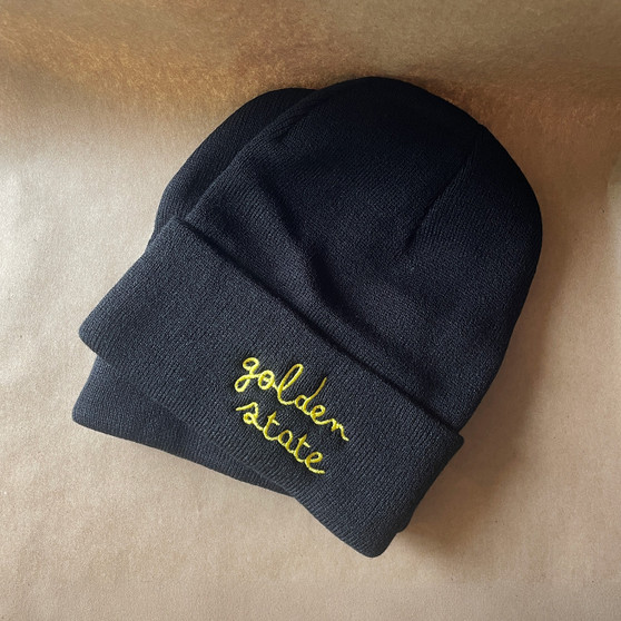 "Golden State" embroidered in cursive in yellow onto a black beanie