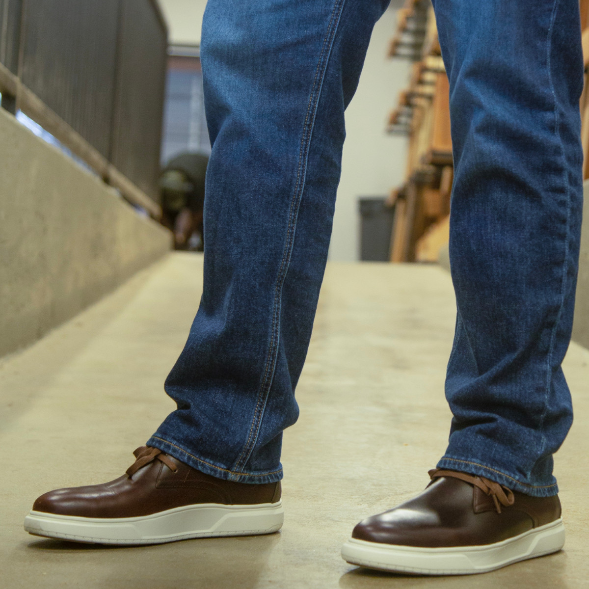 Premier Work Men's Dark Cognac Casual Work Chukka - FS2334 Close-up of a person wearing Premier Work Men's FS2334 Dark Cognac Casual Work Chukka boots, styled with jeans on a concrete ramp.