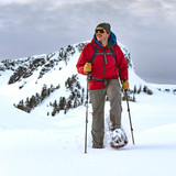 Man trekking through mountain snow wearing red jacket and Crescent Moon snowshoes, using poles Man trekking through mountain snow wearing red jacket and Crescent Moon snowshoes, using poles