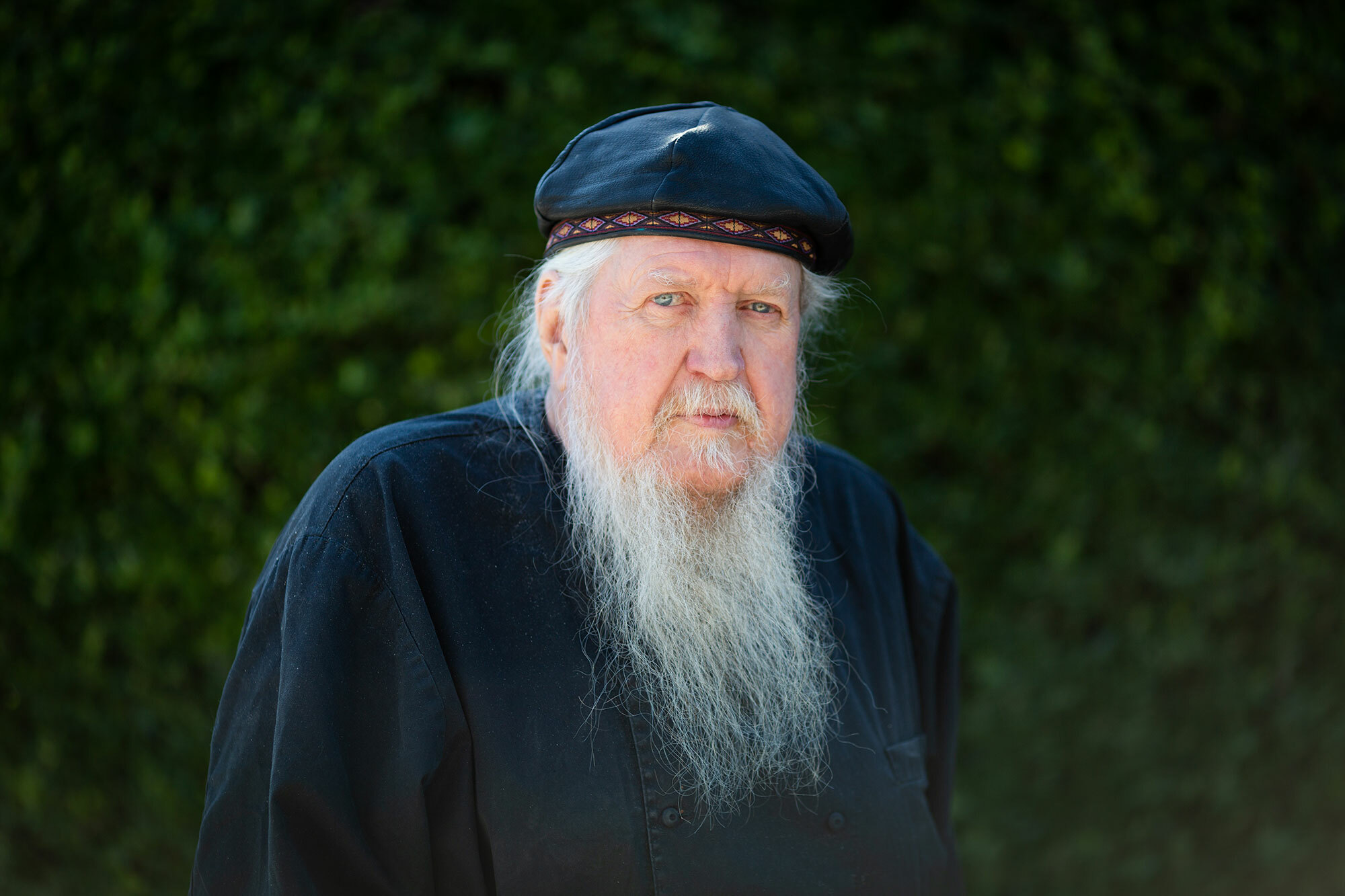 Portrait of the artist Michael Mentler. He is an elderly gentleman with silver hair, mustache, and beard. He is wearing a black shirt and a black beret.