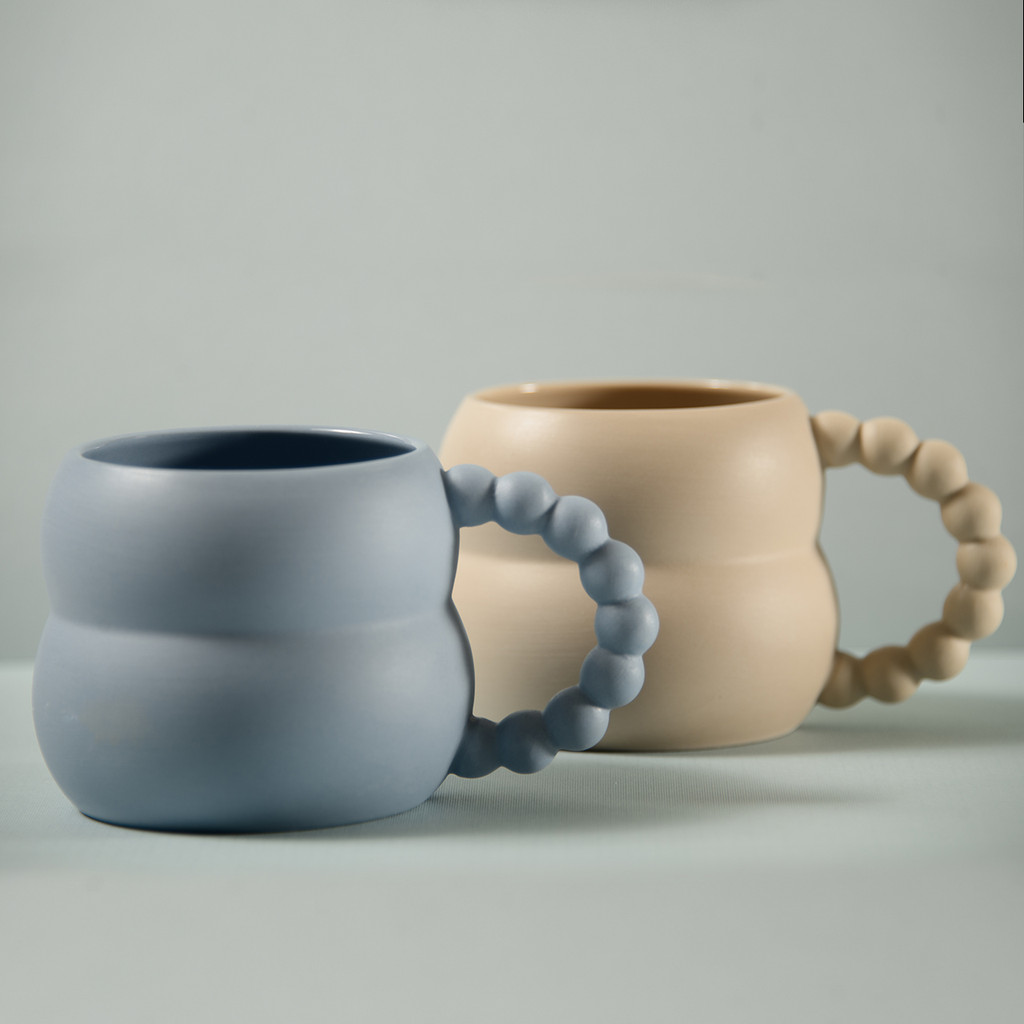 a Blue and an off-white mug with whimsical beadlike handles