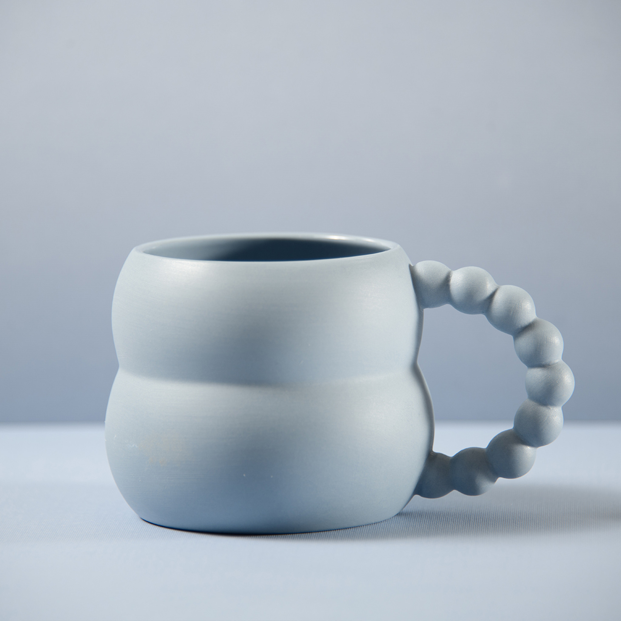 https://cdn11.bigcommerce.com/s-ps4uyod7mi/images/stencil/2048x2048/products/2105/2437/Blue_mug_with_whimsical_beadlike_handles_tan_background_1280__50525.1665244602.jpg?c=2