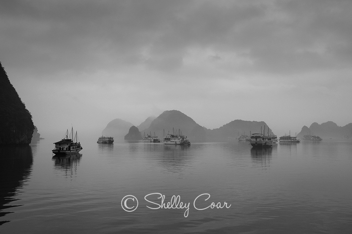 A black and white photograph of the boats of Halong Bay, Vietnam in the morning mist by Shelley Coar.