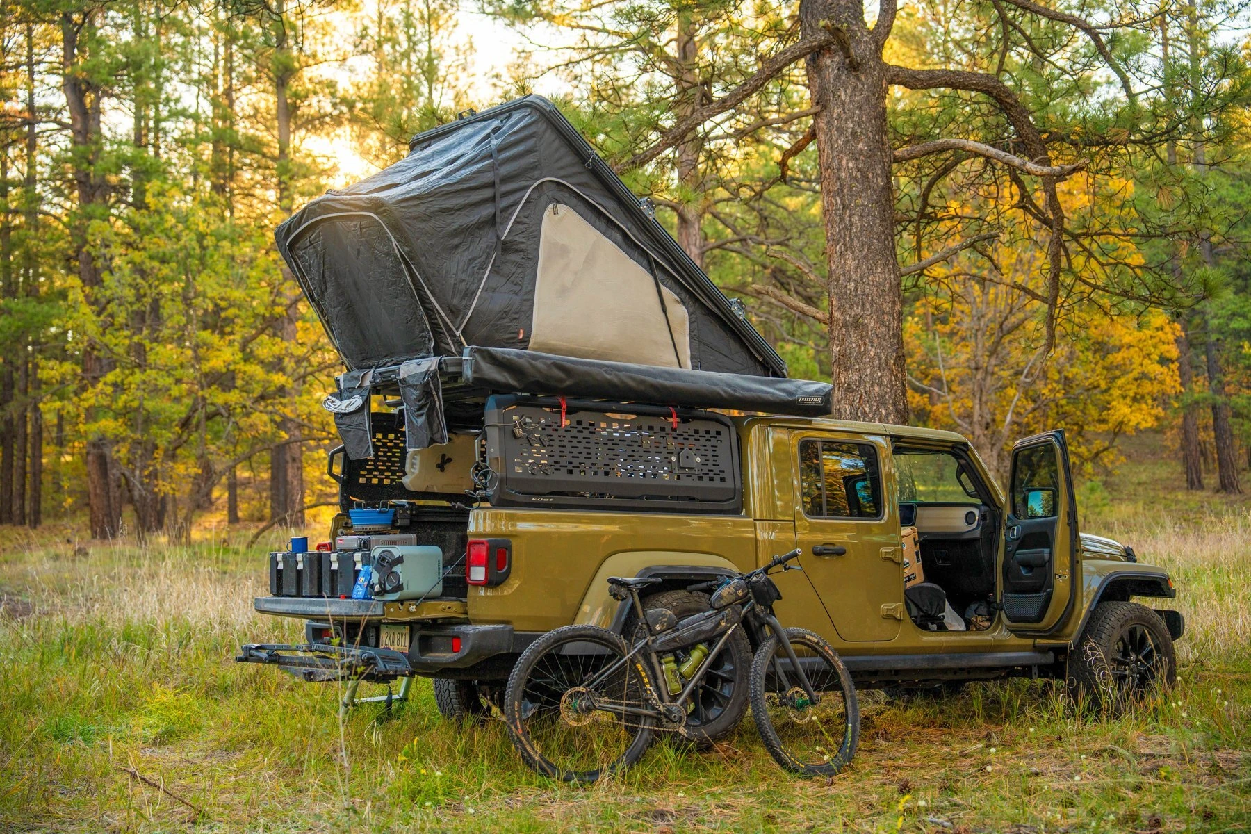 A rooftop tent and mountain bike at camp in the autumn forest.