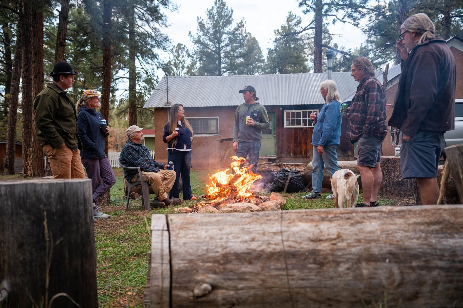 Riders gather around a campfire outside a cabin.