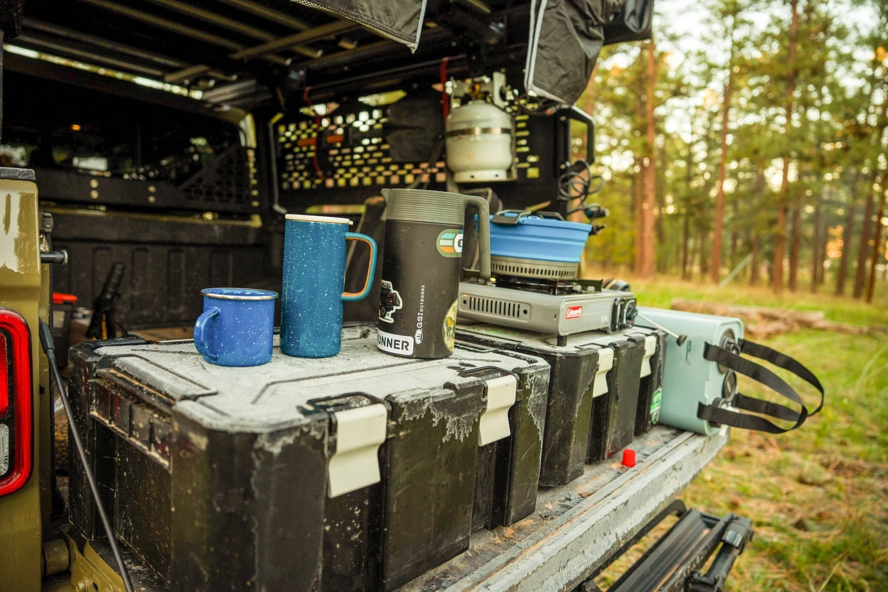 Camp coffee setup on the tailgate beneath the trees.