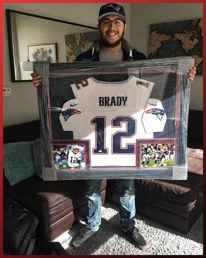 A man holding a framed Tom Brady Patriots jersey