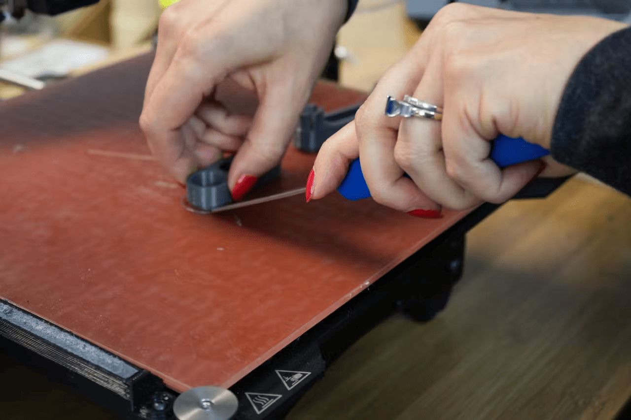 photo of hand lifting 3d print off of the 3d printer bed  using a tool to get underneath the printed object