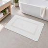 A white microfiber bath rug on the floor in a bathroom.