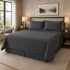 A dark gray color quilted coverlet set on a hotel bed.