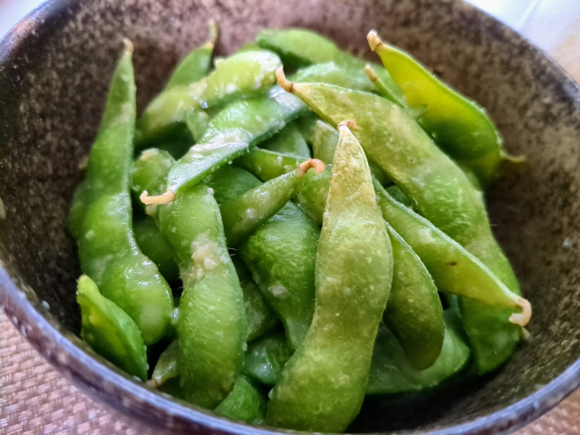 Green edamame pods in a dark, textured ceramic bowl.