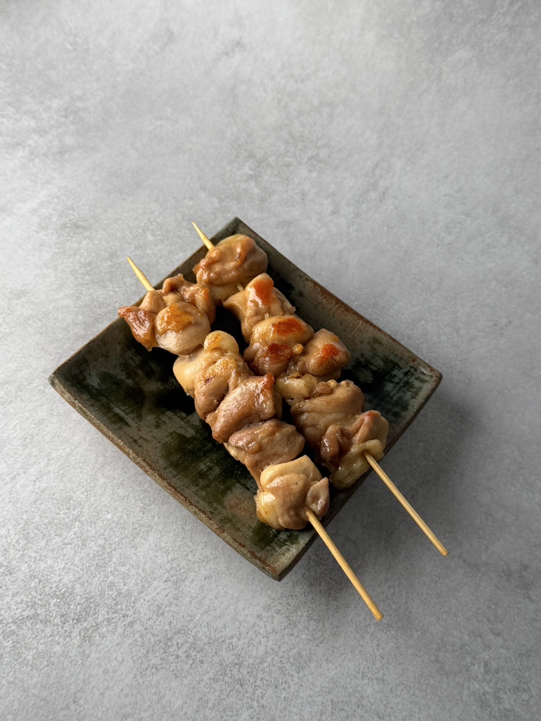 Another angle of two grilled chicken skewers on a glazed rectangular ceramic plate.