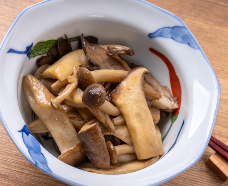 A mix of cooked mushrooms in a white patterned ceramic bowl on a wooden table.