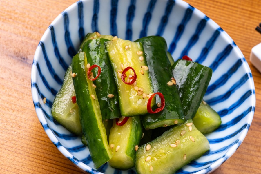 Pieces of cucumber with sesame seeds and red chili rings in a bowl with blue stripes.