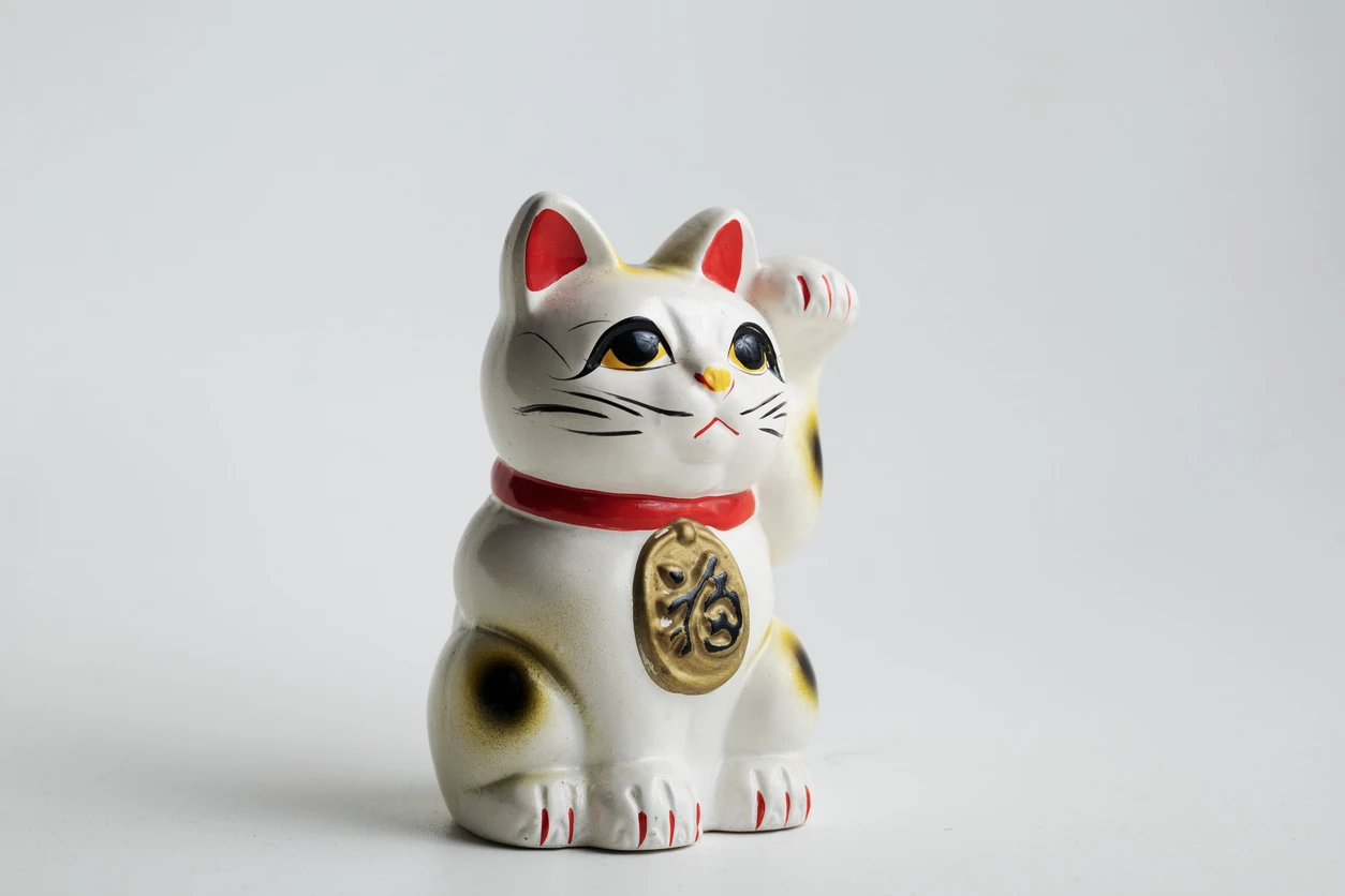 Calico maneki neko with right paw raised, holding a gold koban inscribed with the kanji for fortune, in classical Tokoname style