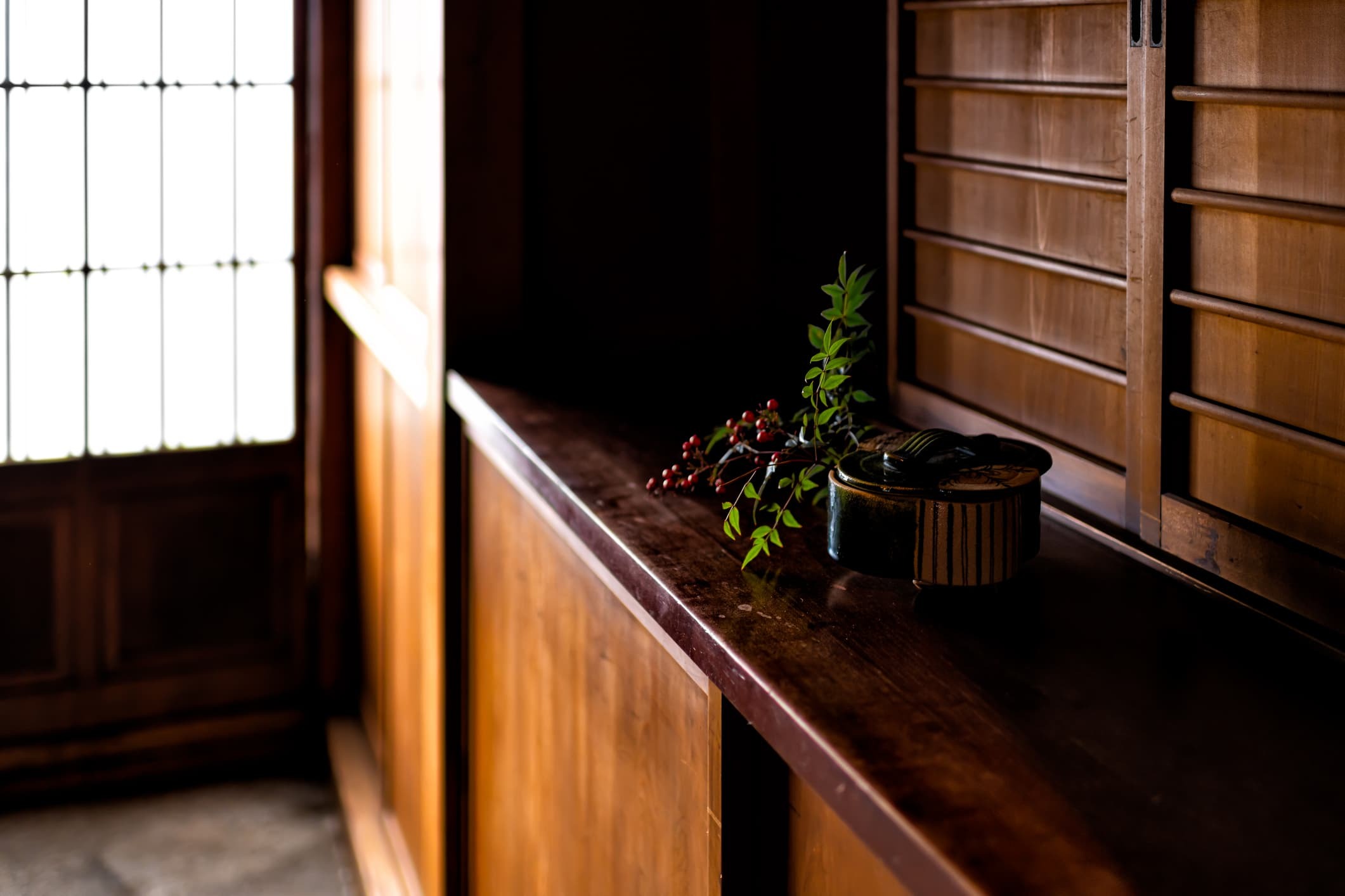 Wooden shelf in an old Japanese house with small ceramic vessels and a red-berry branch
