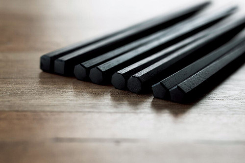 Black urushi-lacquered heptagonal chopsticks resting on a wooden table, showing the deep soft sheen of natural lacquer