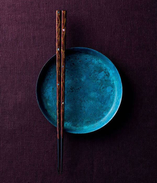 A pair of Wakasa-nuri lacquered chopsticks resting on an indigo dish over deep purple linen