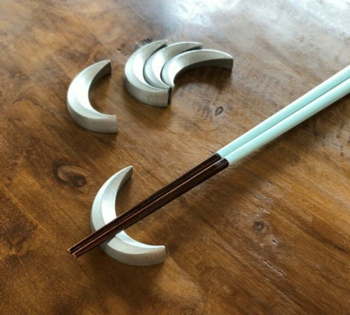 Cast tin crescent-moon chopstick rests holding a pair of chopsticks on a wooden table