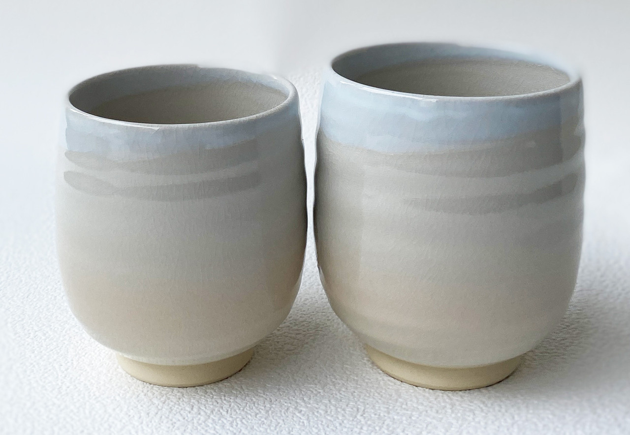 A pair of Hagi-ware yunomi teacups in a soft blue-to-cream gradient glaze, standing side by side